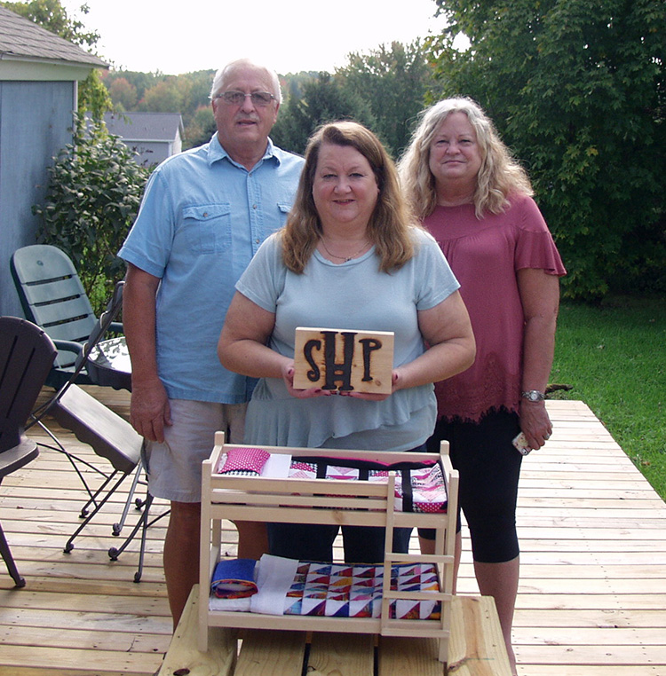 Sid Sinnema, Sue Thompson, and Aurene Sinnema display the SHP brand and a small version of a bunk bed Sid built.