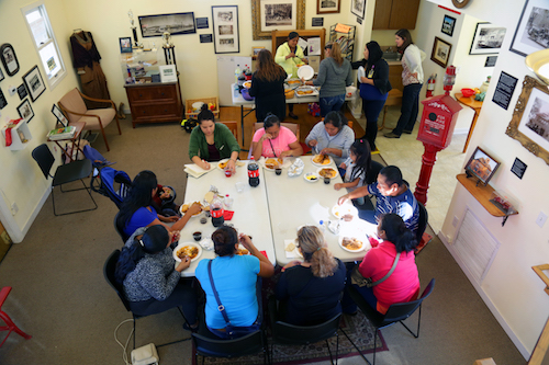 Miembros de la comunidad comparten una comida juntos en el edificio del la Asociación del Vecindario Roosevelt.