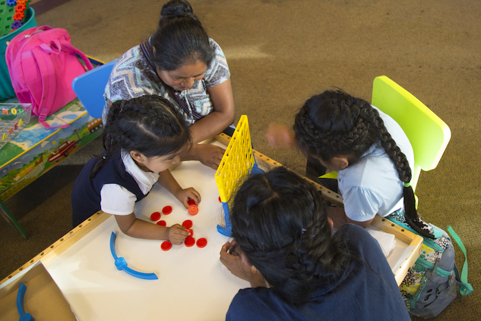 Dominga Lucas-Pérez plays a game of connect four with her three daughters at the Cook Library Center on Grandville Avenue.