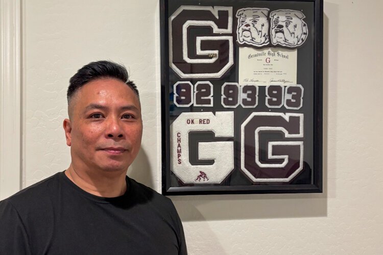 Jennifer Pham’s father, Thong Pham, stands beside his Varsity Letter awards in soccer, wrestling, and track from Grandville High School (2025).