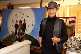 Artist Paul Collins in his studio with his signature cigar and favorite leather hat.
