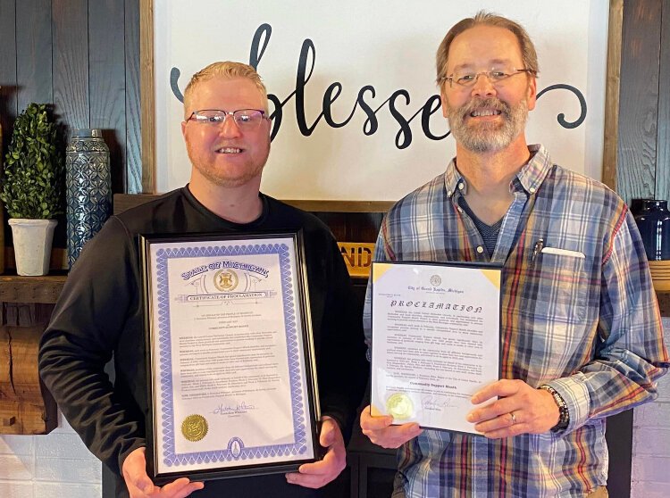 Davin Risk (left) and the Rev. Brad Brillhart from Lowell United Methodist Church hold copies of a proclimation from Gov. Gretchen Whitmer, declaring February “Community Support Month” in Michigan.